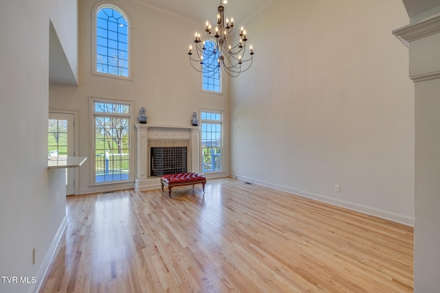 unfurnished living room featuring a towering ceiling, light hardwood / wood-style floors, a notable chandelier, and crown molding