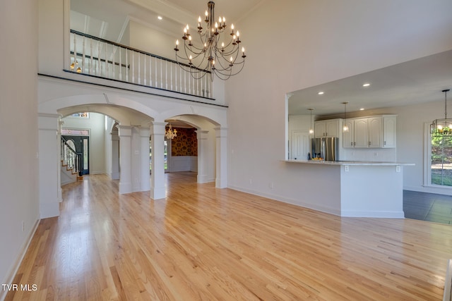 unfurnished living room with a high ceiling, light wood-type flooring, ornamental molding, and decorative columns