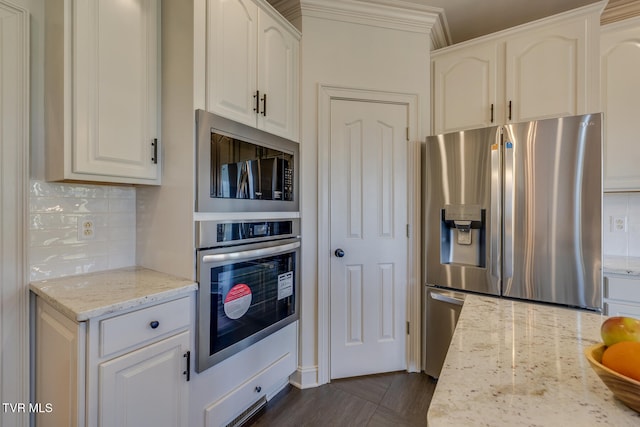 kitchen with white cabinetry, stainless steel appliances, backsplash, and light stone countertops