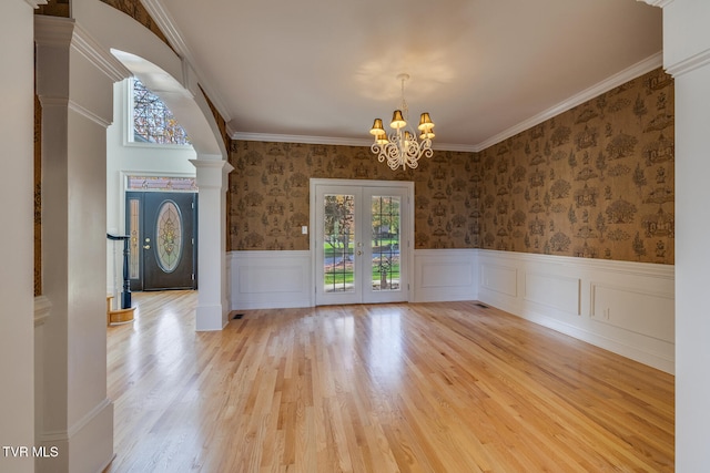 unfurnished dining area with french doors, ornamental molding, light wood-type flooring, ornate columns, and a chandelier