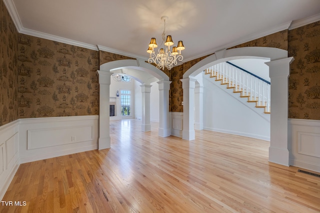 unfurnished dining area featuring ornamental molding, a notable chandelier, light wood-type flooring, and decorative columns