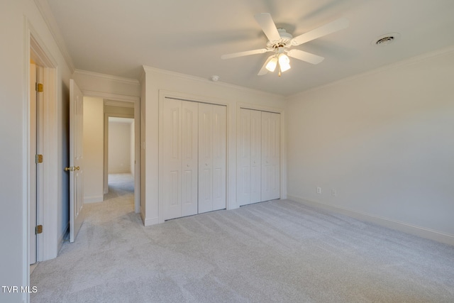 unfurnished bedroom with light colored carpet, ceiling fan, multiple closets, and ornamental molding