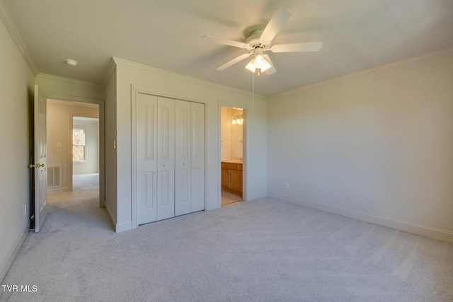 unfurnished bedroom featuring a closet, ensuite bath, crown molding, light colored carpet, and ceiling fan