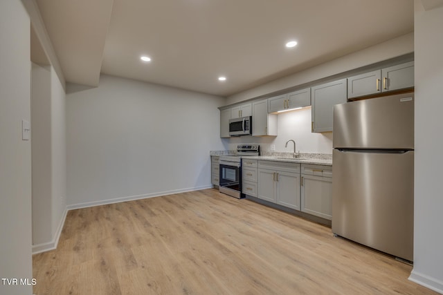 kitchen featuring appliances with stainless steel finishes, gray cabinets, light stone countertops, sink, and light hardwood / wood-style flooring