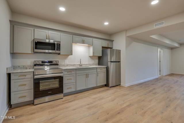 kitchen featuring sink, appliances with stainless steel finishes, light stone countertops, light hardwood / wood-style flooring, and gray cabinetry