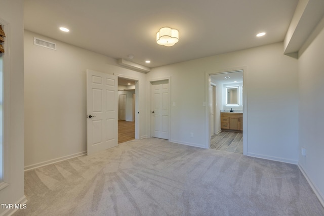 unfurnished bedroom featuring light carpet and ensuite bath