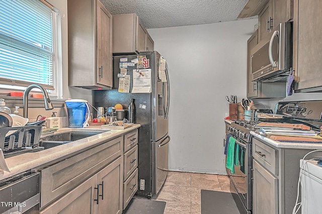 kitchen featuring light tile patterned floors, a textured ceiling, stainless steel appliances, and sink