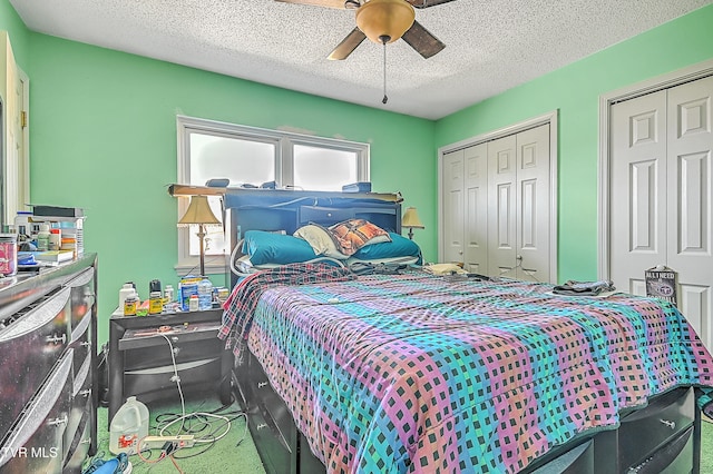 carpeted bedroom with ceiling fan, a textured ceiling, and two closets