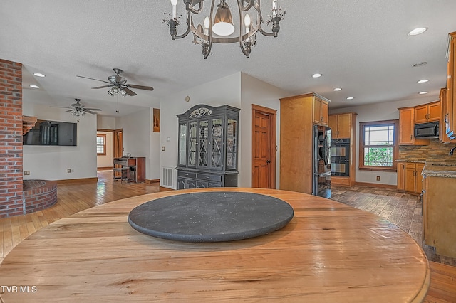 dining space with ceiling fan with notable chandelier, a textured ceiling, and light wood-type flooring