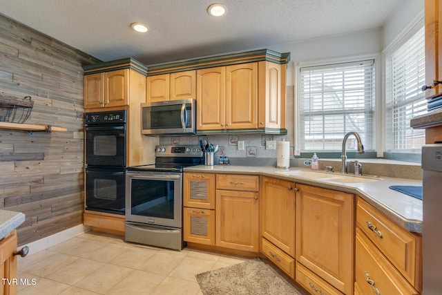 kitchen with wood walls, sink, stainless steel appliances, and a textured ceiling