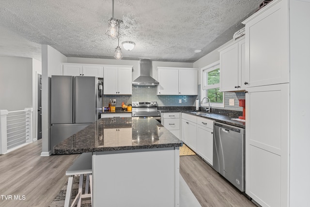 kitchen featuring wall chimney exhaust hood, stainless steel appliances, sink, light hardwood / wood-style floors, and a kitchen island