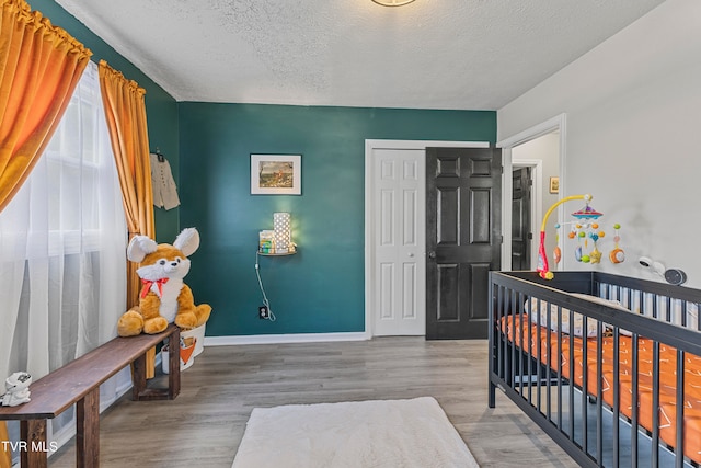 bedroom with a crib, hardwood / wood-style floors, a textured ceiling, and a closet