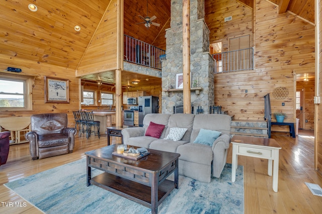 living room with light hardwood / wood-style flooring, high vaulted ceiling, and wooden walls