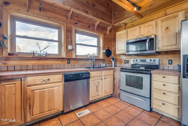 kitchen with beam ceiling, sink, tile countertops, light tile patterned floors, and appliances with stainless steel finishes