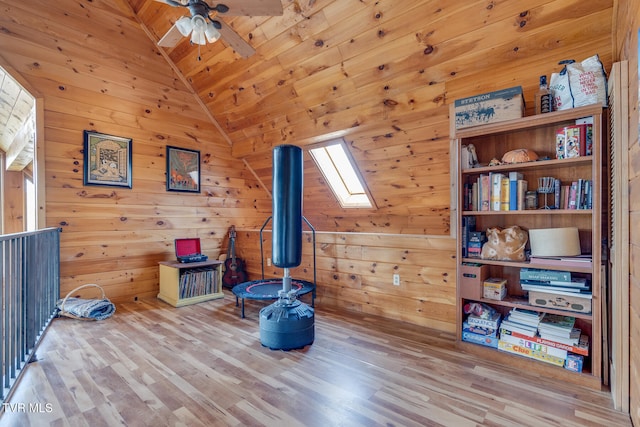 misc room featuring light wood-type flooring, vaulted ceiling with skylight, ceiling fan, and wood walls