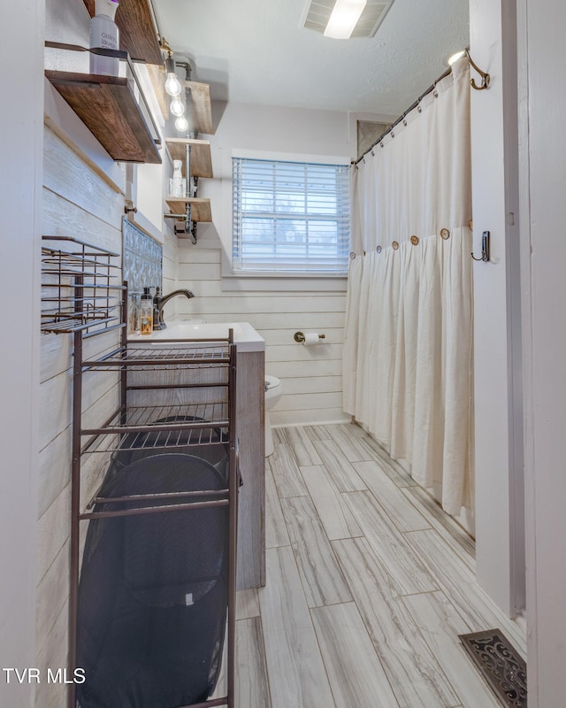 bathroom with a textured ceiling, sink, toilet, and wood walls