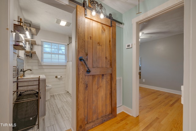 bathroom with ceiling fan, wood walls, wood-type flooring, toilet, and vanity