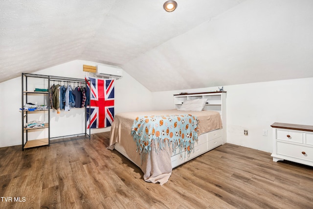 bedroom featuring hardwood / wood-style floors, lofted ceiling, and a wall mounted AC