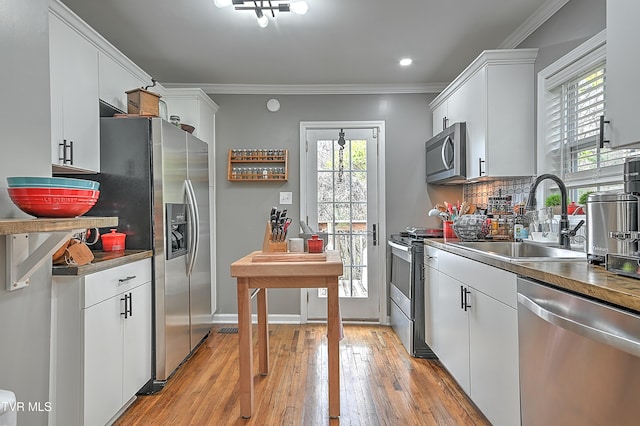 kitchen featuring appliances with stainless steel finishes, tasteful backsplash, sink, light hardwood / wood-style flooring, and white cabinets