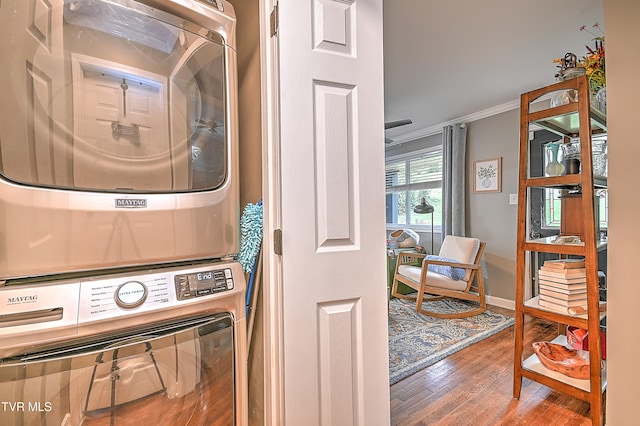 clothes washing area with crown molding, wood-type flooring, and stacked washer and clothes dryer