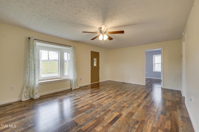 empty room featuring a textured ceiling, a wealth of natural light, dark wood-type flooring, and ceiling fan