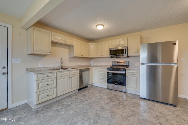 kitchen featuring a textured ceiling, stainless steel appliances, light stone counters, and sink