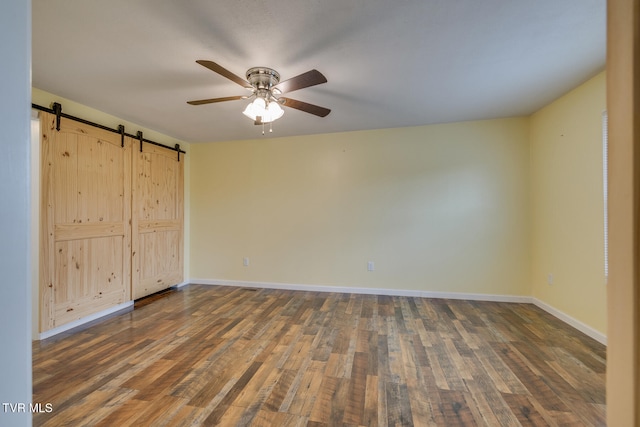 unfurnished bedroom with ceiling fan, dark hardwood / wood-style floors, and a barn door