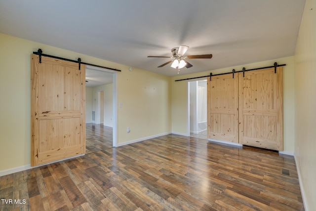 unfurnished bedroom featuring a barn door, dark hardwood / wood-style floors, and ceiling fan