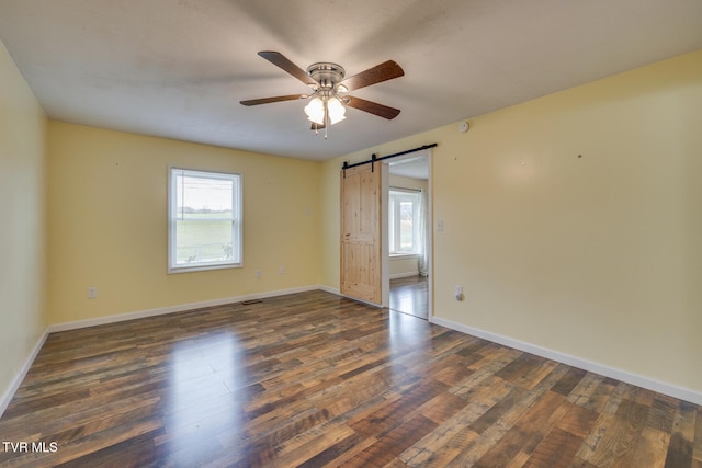 empty room with a barn door, ceiling fan, and dark wood-type flooring