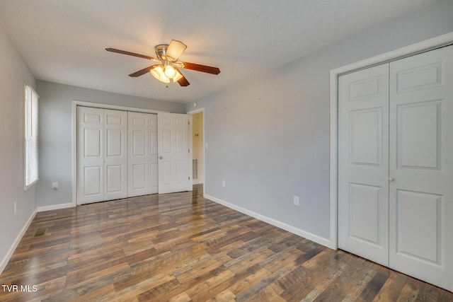 unfurnished bedroom featuring multiple closets, ceiling fan, and dark wood-type flooring