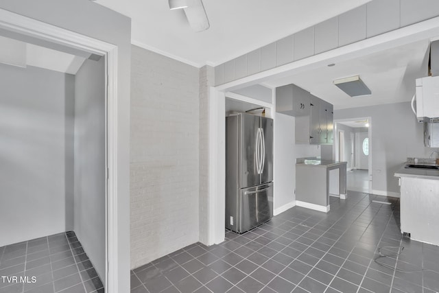 kitchen with brick wall, dark tile patterned floors, sink, and stainless steel refrigerator