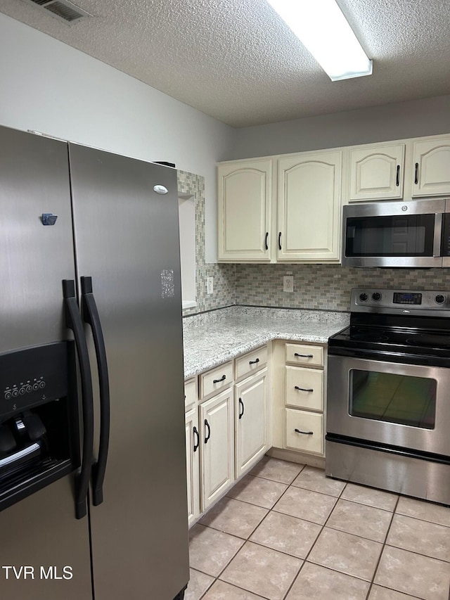 kitchen with cream cabinetry, decorative backsplash, light tile patterned floors, and appliances with stainless steel finishes