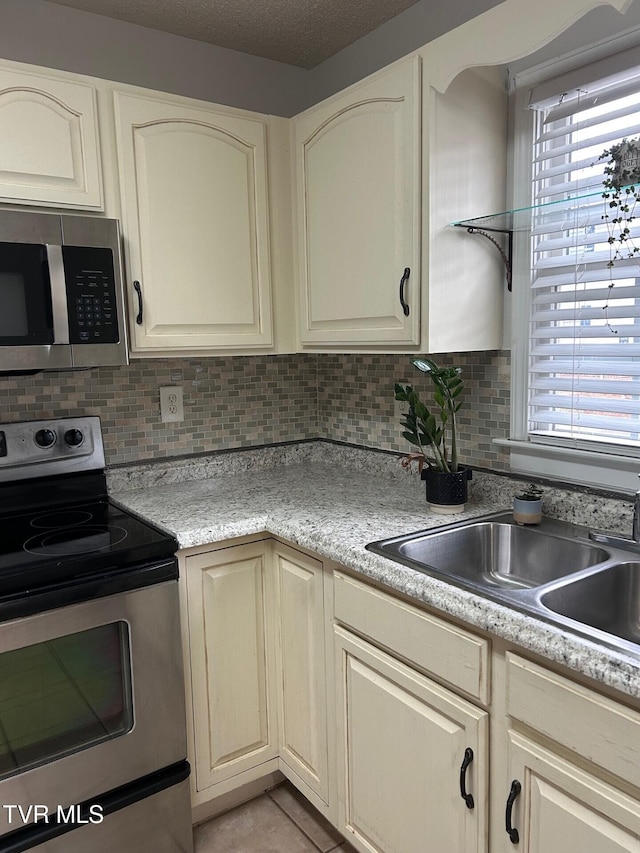 kitchen with cream cabinets, stainless steel appliances, tasteful backsplash, and sink