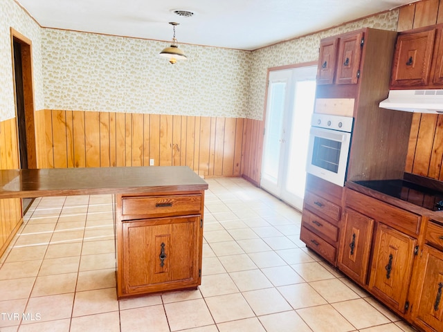 kitchen featuring hanging light fixtures, wood walls, oven, extractor fan, and light tile patterned floors