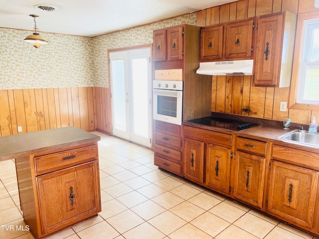 kitchen featuring wood walls, black electric stovetop, oven, sink, and hanging light fixtures