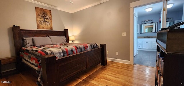 bedroom featuring light hardwood / wood-style flooring, ensuite bath, ornamental molding, and sink