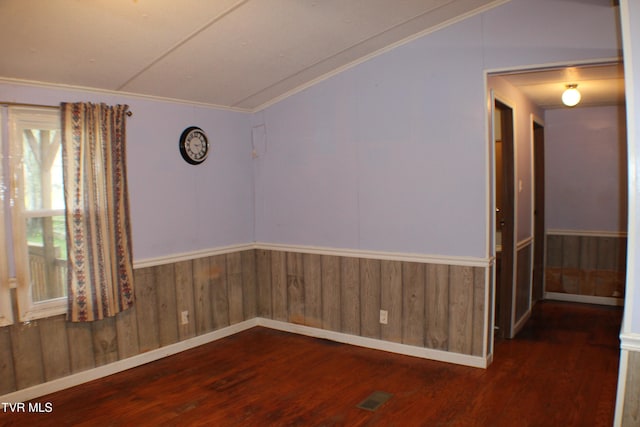 spare room featuring dark hardwood / wood-style flooring, vaulted ceiling, ornamental molding, and wood walls