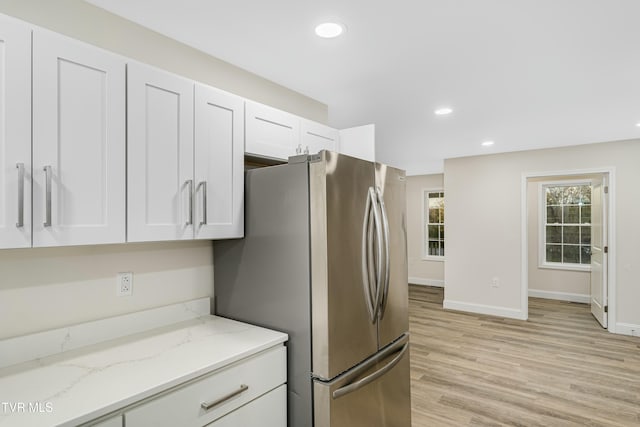 kitchen featuring white cabinets, light stone counters, stainless steel refrigerator, and light hardwood / wood-style flooring