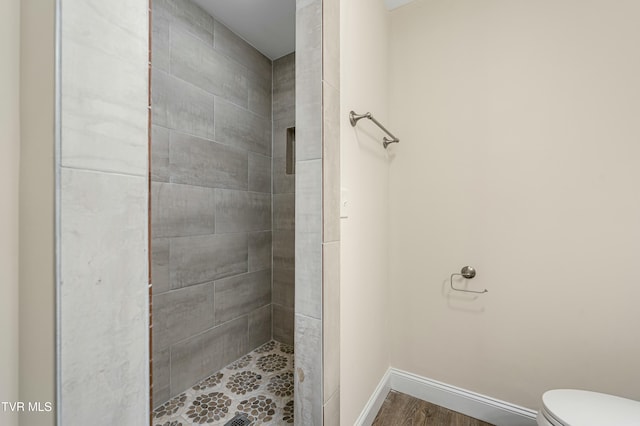 bathroom with wood-type flooring, a tile shower, and toilet