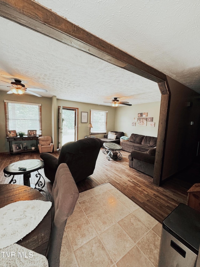 living room featuring light wood-type flooring, beam ceiling, a textured ceiling, and ceiling fan