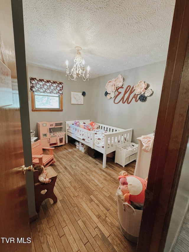 bedroom featuring an inviting chandelier, a nursery area, a textured ceiling, and wood-type flooring