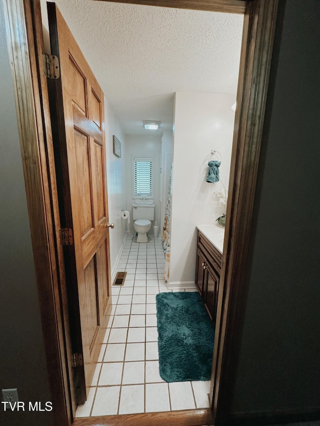 bathroom featuring tile patterned flooring, vanity, a textured ceiling, and toilet