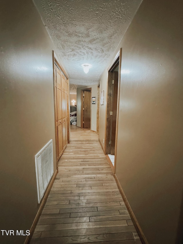 hallway with light hardwood / wood-style floors and a textured ceiling