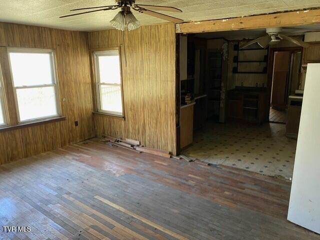 empty room featuring ceiling fan, dark wood-type flooring, and wooden walls