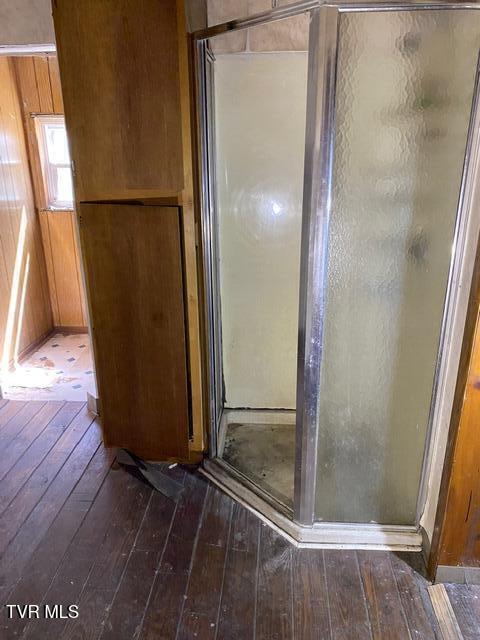 bathroom with hardwood / wood-style floors, an enclosed shower, and wood walls