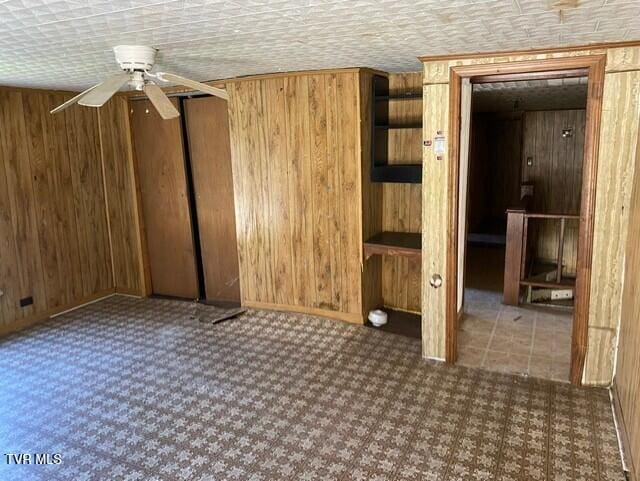 unfurnished room with wooden walls, ceiling fan, and a textured ceiling