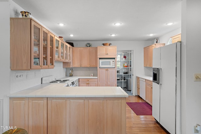 kitchen featuring white appliances, kitchen peninsula, light brown cabinetry, and light hardwood / wood-style flooring