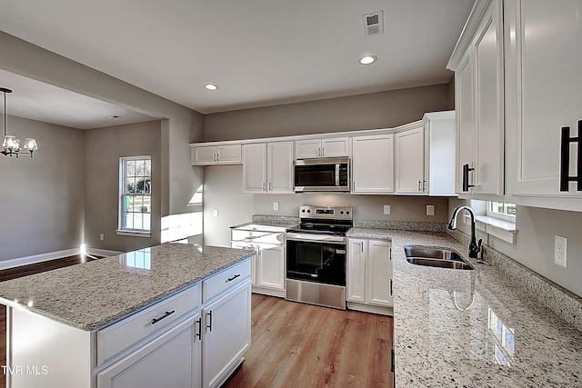 kitchen with sink, hanging light fixtures, stainless steel appliances, white cabinets, and light stone counters