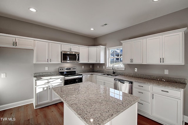 kitchen with stainless steel appliances, a center island, white cabinets, light stone counters, and sink