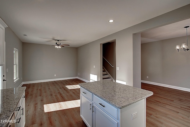 kitchen with white cabinetry, pendant lighting, ceiling fan with notable chandelier, light hardwood / wood-style flooring, and light stone counters